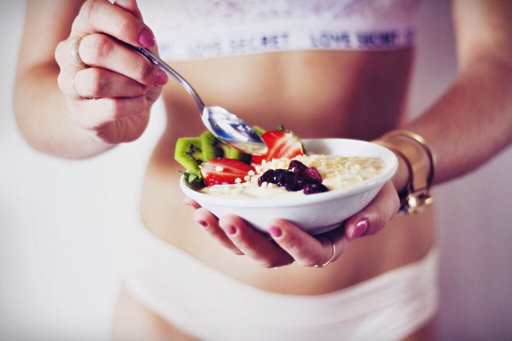 A woman in white underwear holding a bowl of oatmeal and fruit.